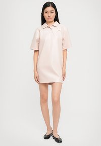 Rochie stil polo din imitatie de piele moale, roz deschis, cu maneci scurte si o silueta usor evazata. Prezinta un detaliu cu un mic logo pe piept.
