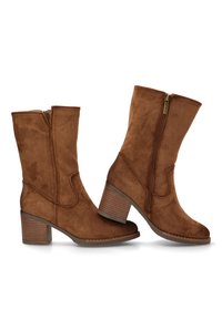 Botas de tobillo de ante marrón con punta redonda, cremallera lateral y tacón apilado. El diseño presenta costuras sutiles y una textura suave.