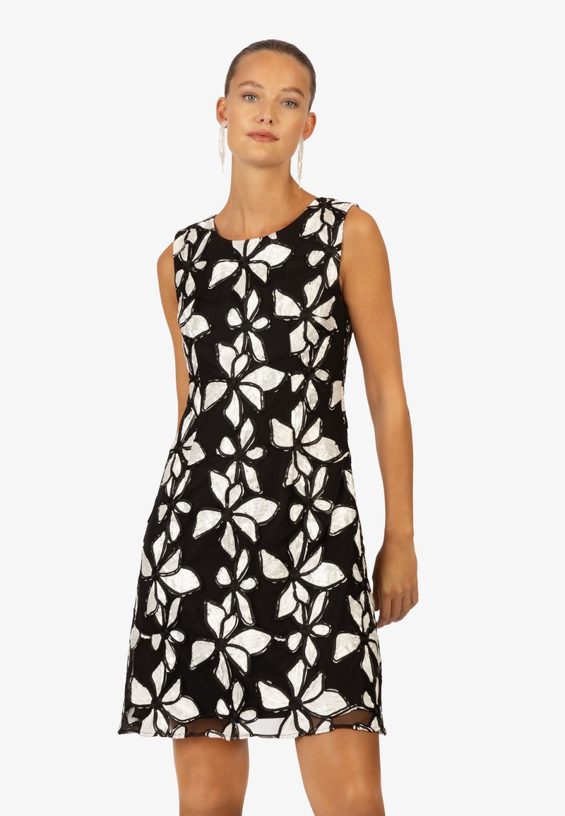 Robe noire sans manches avec broderie florale blanche. Présente un col rond et un tissu texturé. L'ourlet tombe au-dessus du genou.