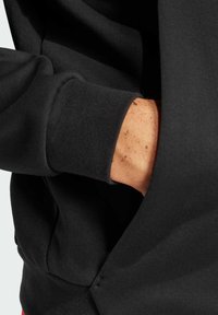 Svart sweatshirt med texturerad tyg, med ribbad mudd och en hand som är tänkt i en känguruficka. Enkel, funktionell design.