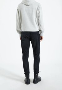 Szara bluza z kapturem o luźnym kroju, w połączeniu z czarnymi zwężającymi się spodniami i czarnymi sznurowanymi butami. Materiał z mieszanki bawełny, minimalistyczny design.