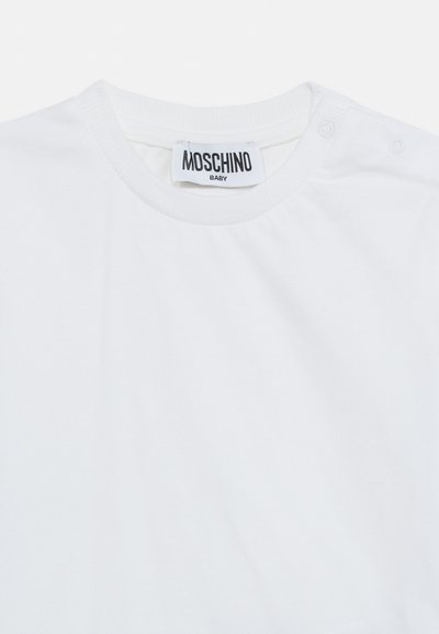 Λευκό παιδικό μπλουζάκι με στρογγυλή λαιμόκοψη, κουμπιά στον ώμο και ετικέτα Moschino Baby στο εσωτερικό του γιακά.