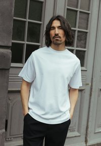 Maglietta bianca a maniche corte realizzata in tessuto liscio, con scollo rotondo, abbinata a pantaloni scuri con motivo.