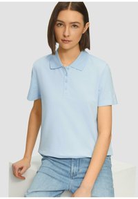 Lichtblauw polohemd met kraag, korte mouwen en een sluiting met vijf knopen. Zachte textuur; recht gesneden, gedragen met lichte denimjeans.