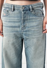 Moderat høyt midje lyseblå denimjeans med lett falming, båret av en person som viser midje og øvre lår, med hender avslappet langs siden.