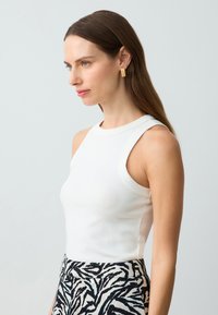 Witte mouwloze top met een ronde halslijn, gecombineerd met high-waisted broek met een zwart-wit zebrapatroon.