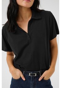 Svart polo skjorta med korta ärmar, knappslå och krage. Bärs tillsammans med en jeanskjol med bälte, vilket visar en avslappnad look.