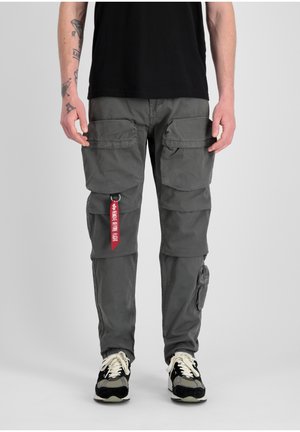 Grijze cargobroek van stof met meerdere voorzakken, een zijzak en een rode label. Gstyliseerd met zwart-witte sneakers.