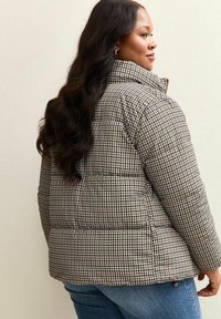 Giubbotto imbottito con motivo a chevron in marrone e beige, con colletto alto e texture trapuntata, abbinato a jeans blu.