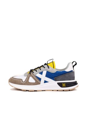 Zapatillas deportivas multicolores que presentan ante gris, malla azul, detalles en blanco, una lengüeta amarilla en el talón y una suela gruesa blanca y negra.