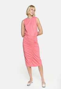 Różowa sukienka z okrągłym dekoltem, bezrękawowa, z marszczonym detalem w talii. Modelka połączyła ją z srebrnymi balerinami.