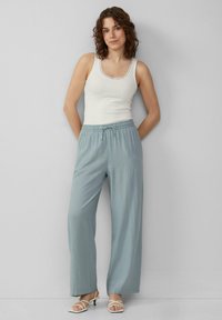 Pantalons larges bleu clair avec une taille à cordon, associés à un débardeur blanc avec un décolleté en dentelle. Texture de tissu lisse.