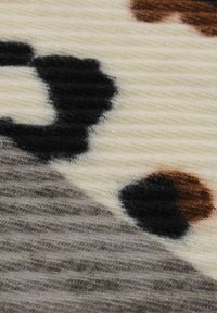 Strukturierter Stoff mit einem abstrakten Muster, das große schwarze, braune und graue Flecken auf einem cremigen Hintergrund zeigt. Weiche und gestrickte Optik.