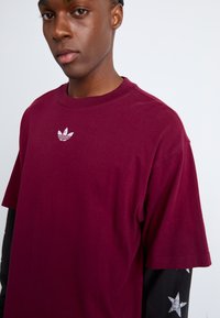 Bordeaux katoenen T-shirt met een ronde hals en korte mouwen. Bevat een klein wit Adidas-logo in het midden. Soepele textuur.