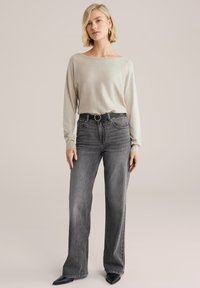 Gai bēšs garu piedurknu tops apvienots ar augsto jostasvietu, platiem pelēkiem džinsiem. Melna josta ar aploka sprādzi un smailām melnām kurpēm noslēdz apģērbu.