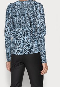 Blusa blu e nera con motivo, dettagli arroshiti, maniche lunghe e orlo posteriore arrotondato. Tessuto morbido con una forma fluida.