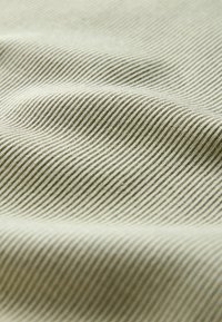 Close-up of beige fabric with fine diagonal ribbed texture and subtle folds creating soft shadows.