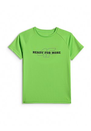 Dziecko stoi, ubrane w zielony t-shirt z napisem "READY FOR MORE", czarne krótkie spodenki, białe skarpetki z czarnymi paskami oraz czarno-białe trampki.