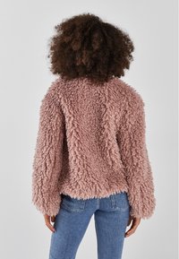Fuzzy, ljusrosa kort topptröja med långa ärmar, texturerad tyg och rak nederkant, parat med blå jeans.