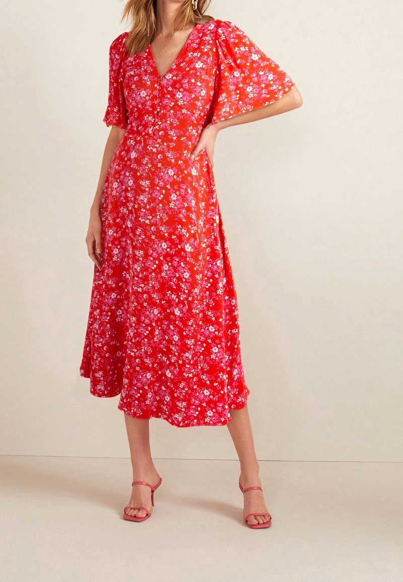Robe midi rouge à fleurs avec des manches courtes bouffantes, un décolleté en V et une jupe fluide, ornée de petits motifs de fleurs roses et blanches.