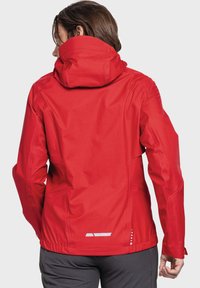 Red waterproof jacket featuring a fully adjustable hood, vertical back pocket, and reflective detailing on the hem and sleeves.