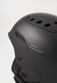 Melna ķivere ar ventilācijas atverēm, uzraksts "Sweet Protection", teksturēta virsma, regulējams siksniņa un elegants, noapaļots dizains.