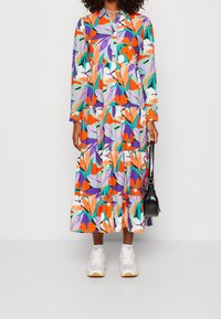 Robe à manches longues et à boutons avec un design en niveaux. Présente un motif floral coloré en orange, violet et vert sur un fond clair.