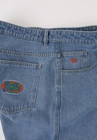 Denimjeans i lyseblå farve med to baglommer og broderede logoer: "Rival Projects" i multifarver og "V7" i rødt.