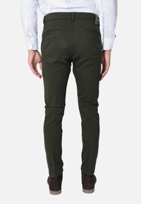 Pantaloni a sigaretta verde oliva realizzati in un tessuto dalla superficie liscia, con due tasche posteriori e una vita cucita. Scarpe marroni completano il look.