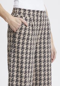 Beige und schwarze Hahnentrittmuster-Hosen mit strukturierter Oberfläche, ausgestattet mit Seitentaschen und einem elastischen Bund.