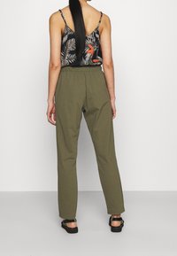 Pantalones elásticos color verde oliva con diseño de pierna recta, combinados con un top de tirantes finos de color oscuro con estampado de hojas de palma.