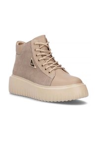 Beżowe sneakersy typu high-top z zamszowymi bokami, sznurowanym przodem, grubą żebrowaną podeszwą i małym trójkątnym metalowym logo po zewnętrznej stronie.