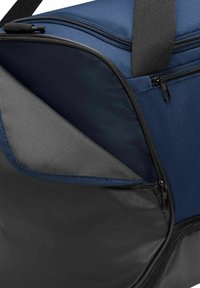 Bolsa de tela azul y gris con un fondo negro. Presenta doble cremallera, exterior texturizado y un gran compartimento abierto que muestra un interior liso.