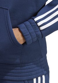 Marineblaue Sweatshirt mit gerippten Bündchen, die über weiße, dreifache Streifen verfügen, einer Fronttasche und einem weichen, strukturierten Stoff.