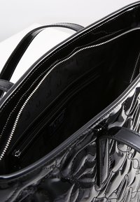 Czarna torebka tote z lakierowanej skóry z wytłaczanym wzorem kwiatowym, zamek błyskawiczny i wewnętrzne kieszenie. Gładka, błyszcząca faktura. Długie uchwyty.