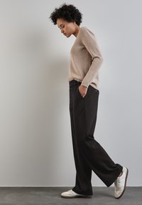 Maglione a maglia beige e pantaloni neri a gamba larga. Il maglione ha una texture a costine. Le scarpe sono bianche con accenti grigi e un design semplice.