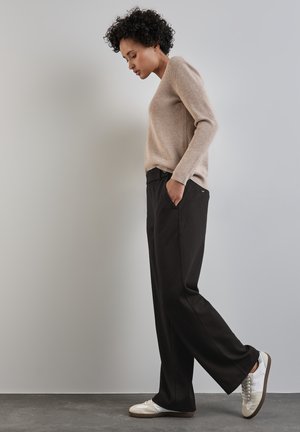 Maglione a maglia beige e pantaloni neri a gamba larga. Il maglione ha una texture a costine. Le scarpe sono bianche con accenti grigi e un design semplice.