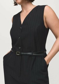 Black sleeveless dress with vertical pinstripes, v-neck design, four buttons, and a belted waist, featuring side pockets and a smooth texture.