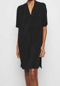Svart kortärmad klänning med V-ringning, tillverkad av mjukt tyg, med subtila veckdetaljer och avslappnad passform, som når till mitten av låret.