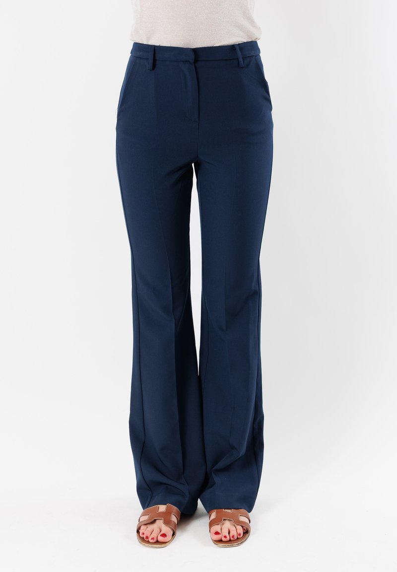 Pantaloni blu navy a vita alta con design a gamba larga e texture liscia. Presenta tasche frontali e delicate pieghe. Indossati con sandali marroni.