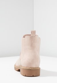 Botín de ante rosa con suela de goma, paneles laterales elásticos y una lengüeta en la parte posterior. El tacón es texturizado y mide aproximadamente 3,8 cm.
