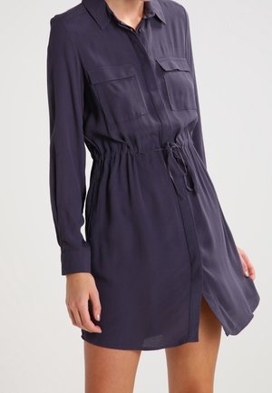 Robe chemise bleue marine à boutons, manches longues, deux poches poitrine, taille cintrée avec cordon de serrage, tissu léger, longueur au-dessus du genou.