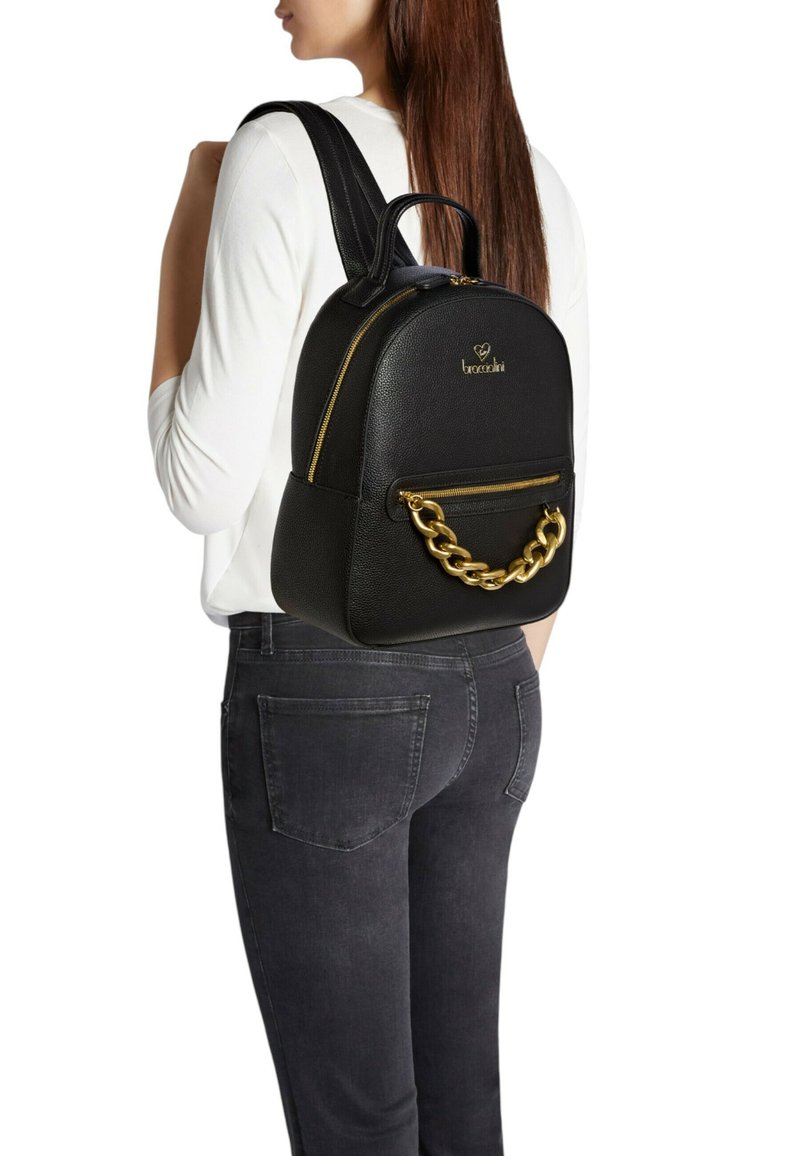 Zaino in ecopelle nera dalla forma arrotondata, con rifiniture dorate e un dettaglio a catena; dotato di due spallacci regolabili e una tasca con cerniera.