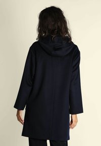 Cappotto blu navy con cappuccio, maniche lunghe e tasche laterali. Realizzato in un tessuto morbido con una texture liscia. Design minimalista con un taglio dritto.