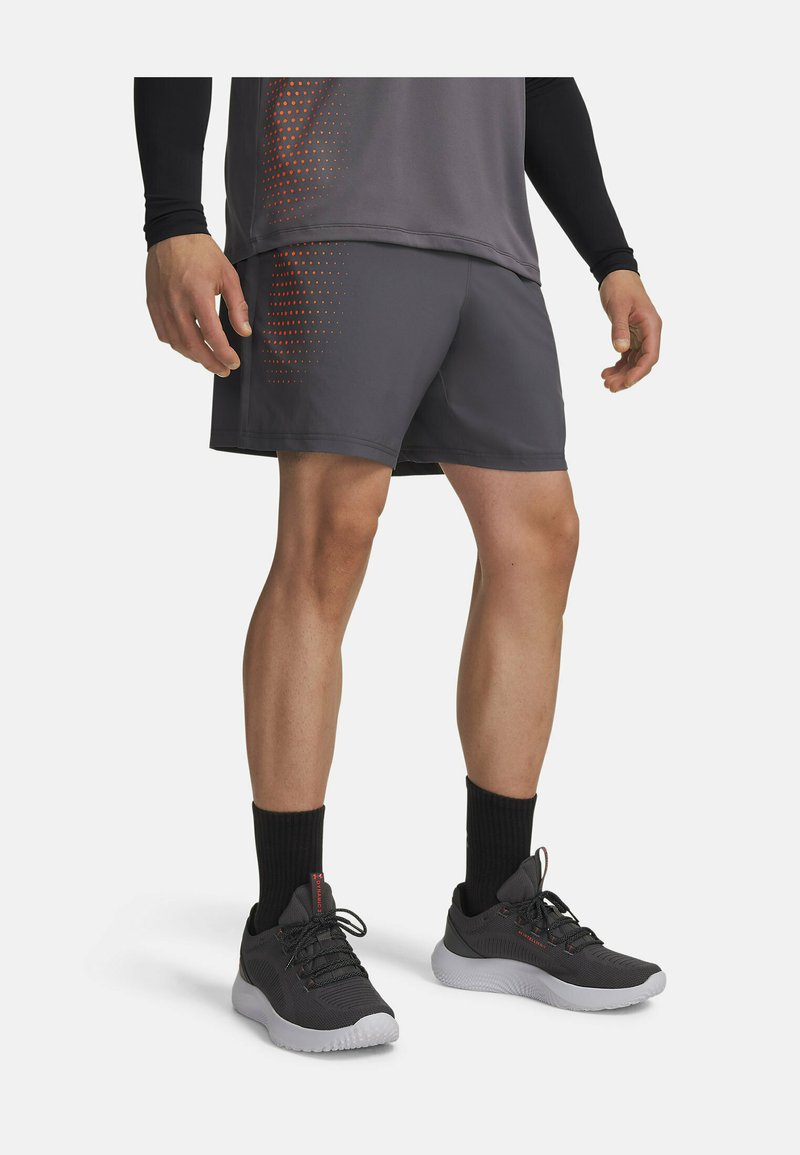 Homme portant un short de sport gris et un t-shirt assorti à pois orange, des chaussettes noires hautes et des chaussures de course noires avec des semelles blanches.