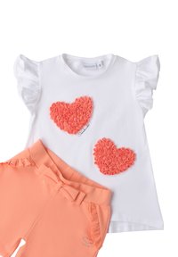 Camisa blanca de manga corta con mangas acampanadas y dos apliques de corazón de color coral, combinada con pantalones cortos coral que presentan un lazo y detalles de volantes.
