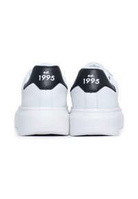 Sneakers bianchi con un'etichetta in pelle nera sul tallone che riporta "est. 1995." Progettati con una texture liscia e una suola in gomma spessa.