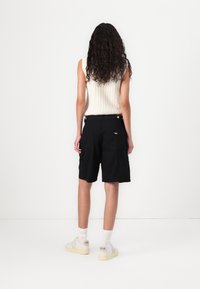 Sorte cargo shorts med flere lommer, fremstillet af letvægtsstof, med en afslappet pasform og parret med hvide sneakers og ankelstrømper.