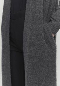 Lång, öppen cardigan i mörkgrått, tillverkad av strukturerat stickat material. Har ribbade ärmslut och sidfickor, lagd över svarta bottenplagg.