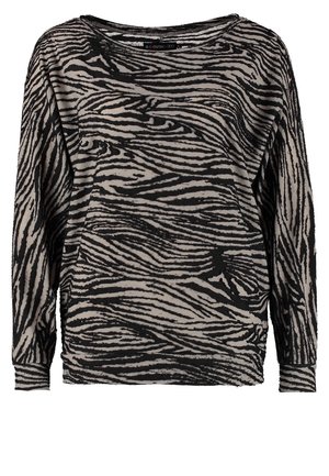 Femme marchant portant un haut manches longues imprimé zèbre noir et gris, un short noir, des sandales à talons hauts noires et tenant une pochette noire.